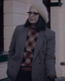 a woman wearing a plaid sweater and a striped jacket is standing in front of a building