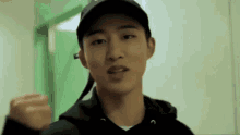 a young man wearing a black hat and a black hoodie is standing in a hallway .