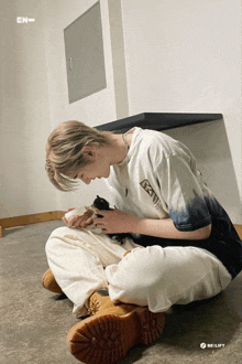 a man is sitting on the floor holding a kitten and wearing a t-shirt that says en on it