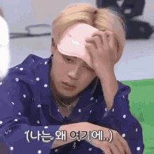 a man wearing a pink hat and a polka dot shirt is holding his head .