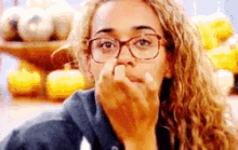 a woman wearing glasses is covering her nose with her finger .