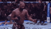 a man without a shirt is standing in a boxing ring with his arms outstretched in front of a crowd .