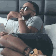 a man is sitting on a bed wearing sunglasses and holding a pen .