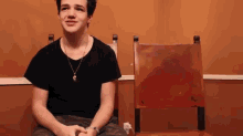 a young man in a black shirt is sitting in a chair with his hands folded