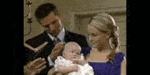 a man and a woman are holding a baby while a priest reads a bible .