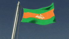 a green and orange flag with arabic writing is flying in the wind