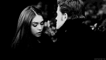 a black and white photo of a man and a woman looking into each other 's eyes .