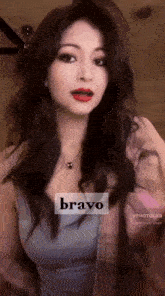 a woman with long hair and red lips is wearing a blue tank top and a plaid jacket .