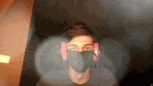 a man wearing a mask and headphones looks at the camera with a blurry background