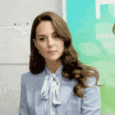 a woman is wearing a light blue jacket and a light blue blouse with a bow tie .