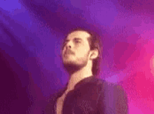 a man with a beard is standing on a stage in front of a pink and blue background .