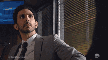 a man in a suit and tie is standing in front of a window with blinds on it ..