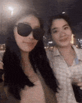 two women wearing sunglasses pose for a picture at night