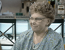 an elderly woman wearing glasses and a pearl necklace smiles
