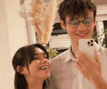 a man and a woman are taking a selfie together . the man is wearing glasses and holding a cell phone .