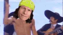 a shirtless man with a bandana on his head is standing next to a man playing a guitar ..