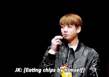 a man in a black jacket is eating chips by himself while standing next to another man .
