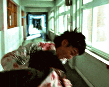 a man in a bloody shirt is standing in a hallway next to a window