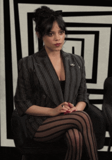 a woman in a suit and striped tights sits on a chair