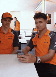 two men wearing orange shirts that say okx are looking at their cell phones