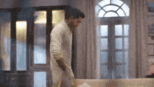 a man in a white shirt is walking towards a couch in a living room .