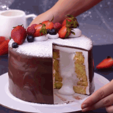a chocolate cake with strawberries and blueberries on top is being cut in half