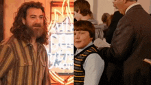 a man with a beard is next to a boy in front of a neon sign that says ' rock ' on it