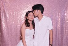 a man kissing a woman on the forehead in front of a pink sequined backdrop