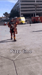 a man in a robot costume is holding a pizza box and says pizza time on the sidewalk