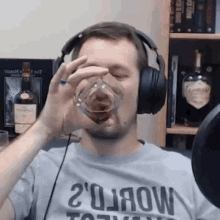 a man wearing headphones and a t-shirt is drinking a glass of whiskey .