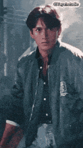 a man wearing a bomber jacket and a black shirt is standing in a dark room .
