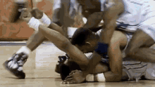 a group of men are wrestling on a basketball court and one of the men is laying on the floor .