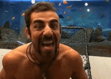 a shirtless man with a beard is standing in front of an aquarium