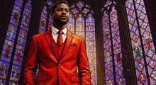 a man in a red suit and tie is standing in front of a church with stained glass windows