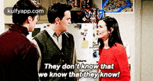 two men and a woman are standing next to each other in a kitchen talking to each other .
