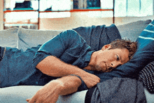 a man in a blue shirt is laying on a couch with his head on his arm .