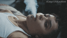 a woman laying on a bed smoking a cigarette with #caughtsstealingmovie written on the bottom