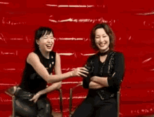 two women are sitting next to each other in front of a red background .