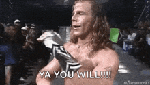 a shirtless wrestler is standing in front of a crowd with the words `` ya you will '' written on his chest .