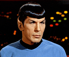 a man in a blue shirt with a black collar is looking at the camera