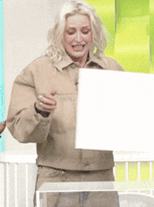 a woman in a tan jacket is holding a white board and smiling