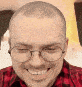 a man wearing glasses and a red plaid shirt smiles