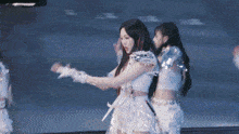 two women are standing next to each other on a stage and one is wearing a white dress