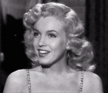 a black and white photo of a woman with blonde hair wearing earrings and smiling .