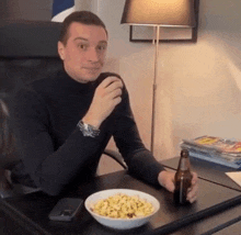 a man sits at a desk with a bowl of food and a beer