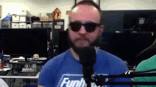a man wearing sunglasses and a funko shirt is talking into a microphone