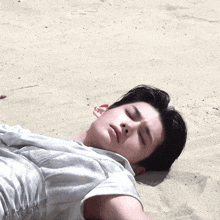 a man in a white shirt is laying on the sand with his eyes closed
