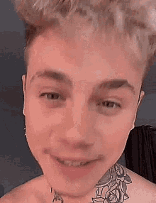 a close up of a young man with a tattoo on his neck smiling .