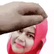 a woman in a red hijab is being patted on the forehead by a hand .