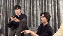a group of young men are sitting on a couch and one of them is pointing at something .